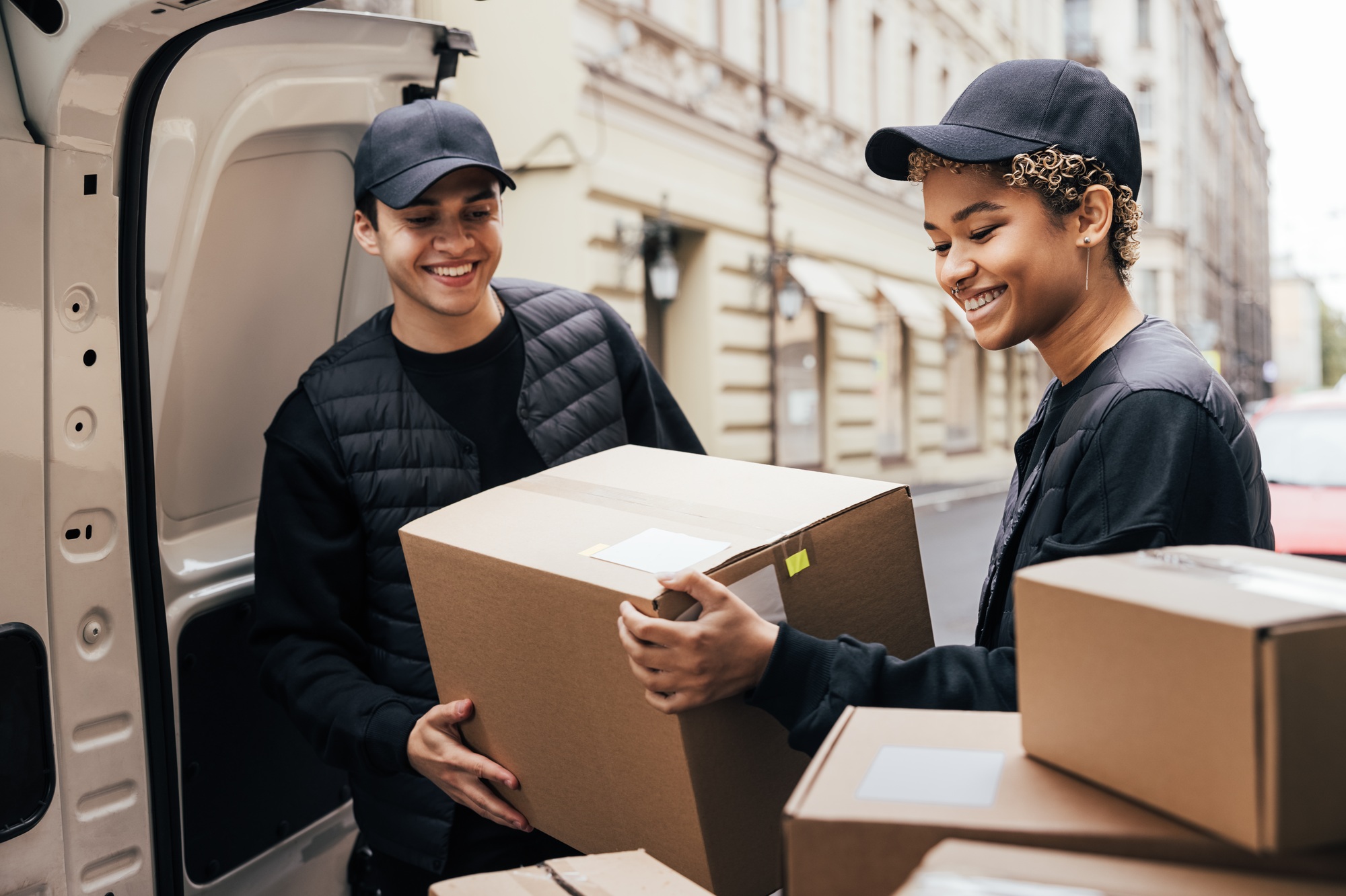 two-smiling-couriers-unloading-cardboard-boxes-from-van-in-the-city
